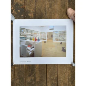 Exhibition poster for Damien Hirst: Pharmacy featuring a wide shot of a sterile, clinical installation with white medicine shelves and glass apothecaries filled with colored liquids.