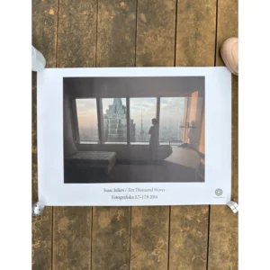 Exhibition poster for Isaac Julien: Ten Thousand Waves at Fotografiska featuring a woman in a hotel room standing by a large window overlooking the Shanghai skyline.