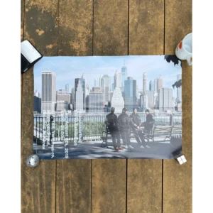 Promotional poster for thisisneverthat FW19 featuring four models in dark varsity jackets seated on a park bench along the East River with the New York City skyline in the background.