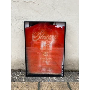 Official Stussy poster featuring iconic handwritten script logo, SS link logo, and world tour chapter cities in white and gold on a vibrant red background, framed in a black aluminum frame, measuring 42x30cm.
