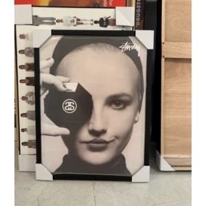 Official Stussy Spring 2019 campaign poster featuring a black and white close-up portrait of a woman holding an octagonal compact mirror with the SS link logo over one eye, framed in a black aluminum frame, measuring 59.5x42cm.
