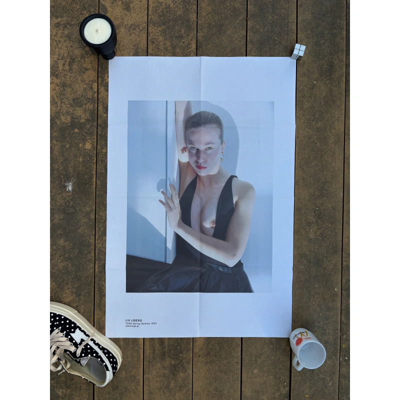 toga ss2023 1 1 Official double-sided TOGA S/S 2023 fashion poster shot by Liv Liberg, featuring a close-up portrait of a woman in a low-cut black dress on Side A, and the same woman seated with red striped tights beside a toddler on Side B, measuring 80.5x53cm.